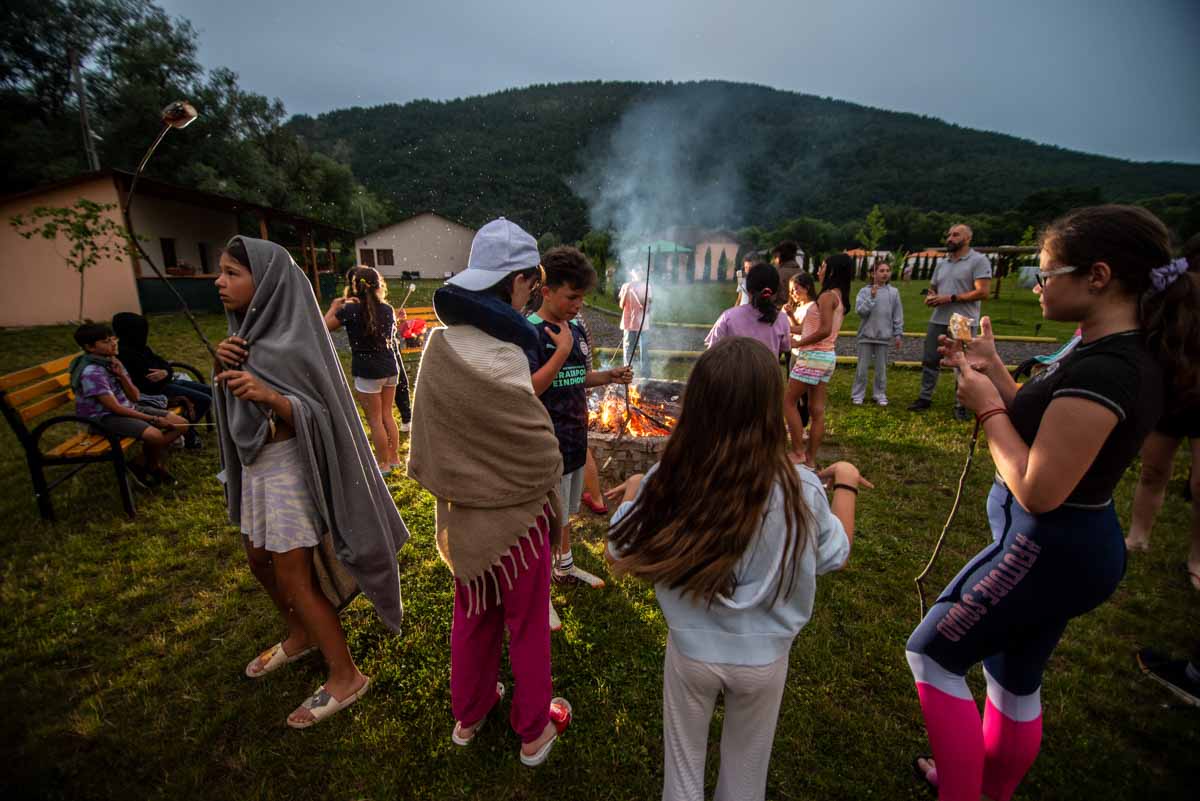 Foc de tabără aprins seara, cu oaspeți adunați în jur
