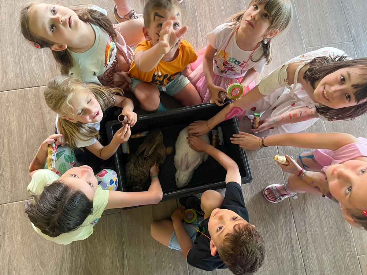 Grup de copii adunați în cerc în jurul unui câine blând, în timpul unei tabere