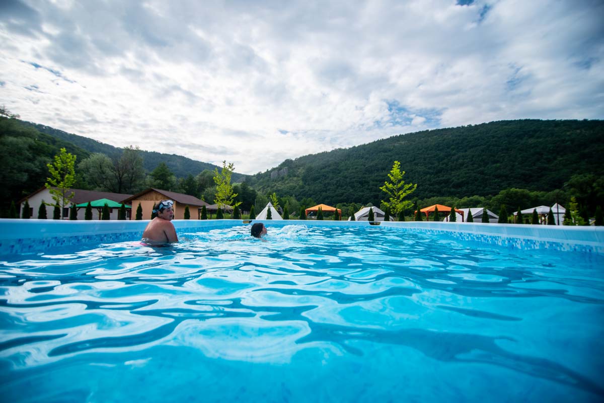 Piscina supraterană plină de oaspeți, cu dealurile Apusenilor în fundal